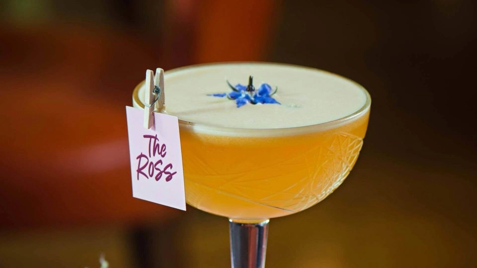 Elegant cocktail garnished with a blue flower in a luxuriously styled bar at The Ross, offering a chic and cosy ambiance.