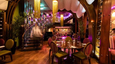 Elegant hotel restaurant with plush seating, spiral staircase, ambient lighting, and wine display, offering a chic dining experience.