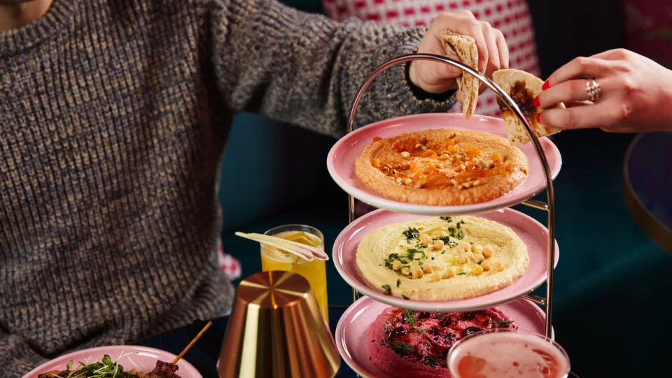 Guests enjoy vibrant hummus trio with cocktails in a cosy hotel lounge, creating a warm, welcoming dining experience.