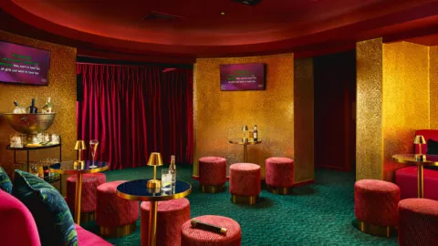 Chic hotel lounge with vibrant red and gold decor, plush seating, karaoke screens, and a selection of drinks for a fun night.