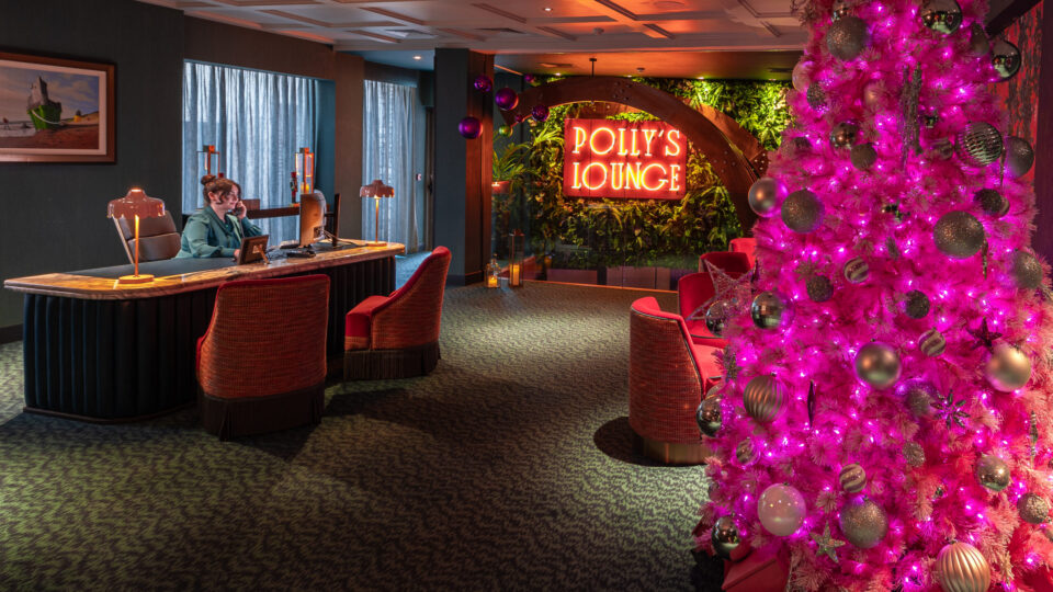 Cosy lounge with pink Christmas tree, neon sign, lush decor, inviting seating, and warm lighting for a welcoming stay.